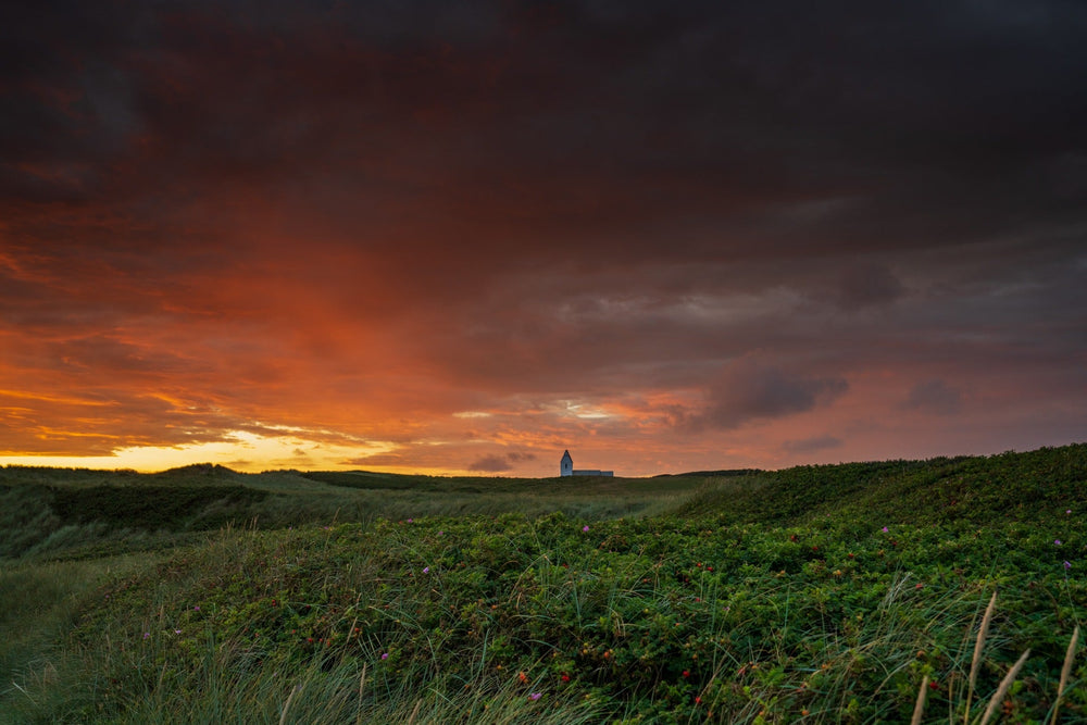 Summer sunset over fields and Trans Kirke church beneath dark clouds — Joseph Hubbard, Hubbard.ART