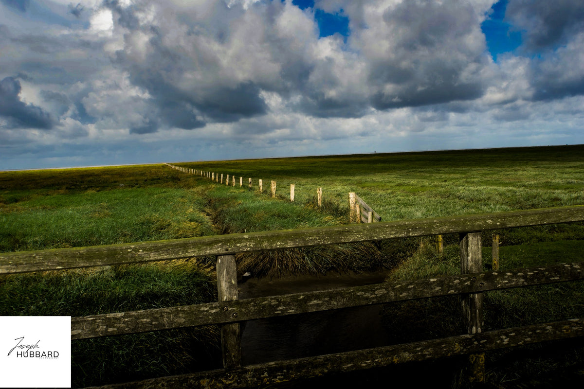 Sunlit fields and a wooden fence beneath approaching storm clouds — Joseph Hubbard, Hubbard.ART
