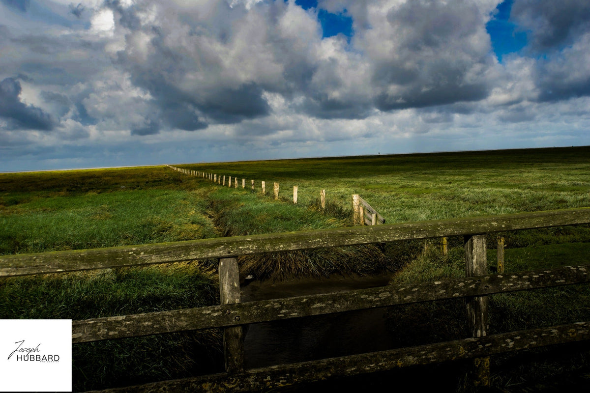 Sunlit fields and a wooden fence beneath approaching storm clouds — Joseph Hubbard, Hubbard.ART